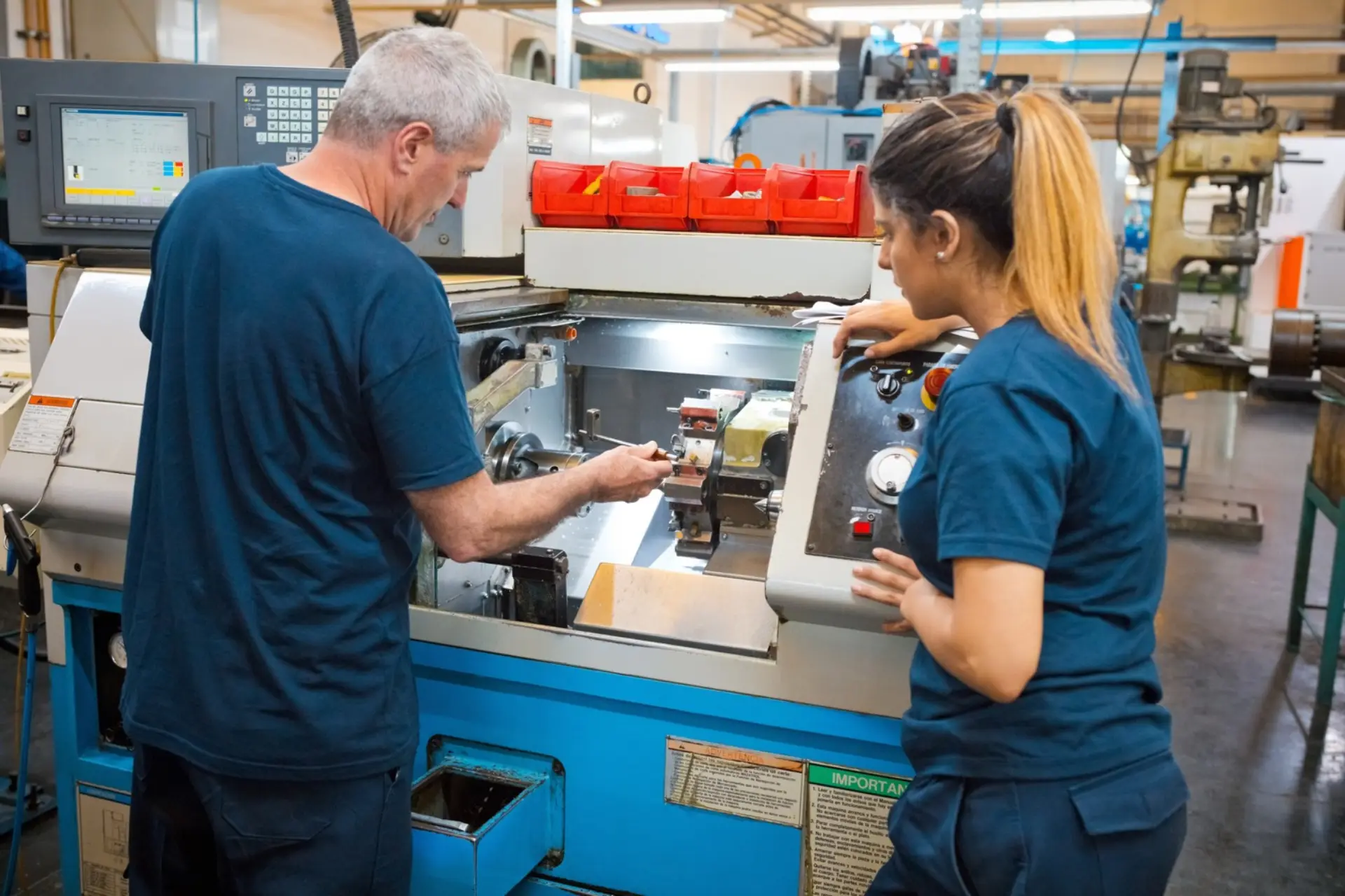 Two machinists reading live job data on a CNC machine control panel